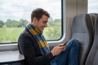 Jeune homme souriant regardant son smartphone dans un train